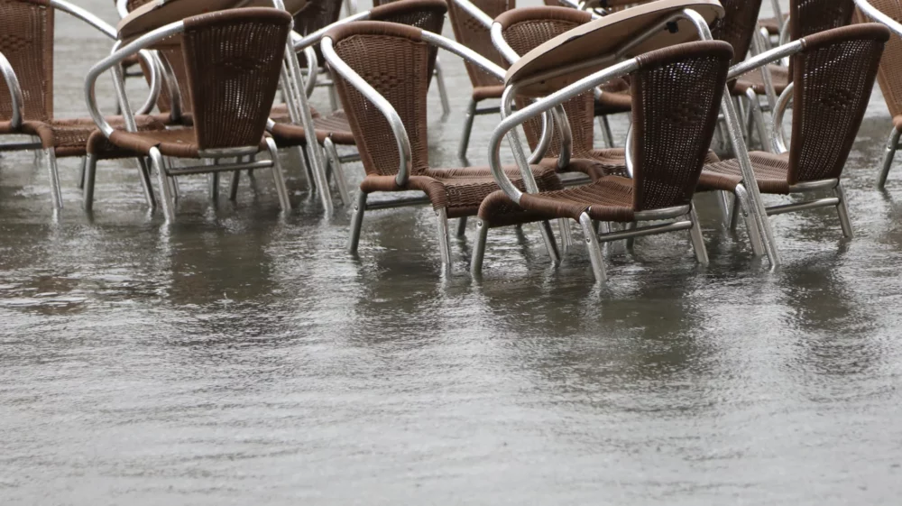 Flooded Venice with a lineup of empty chairs partially submerged in water, highlighting the impact of high tide events.