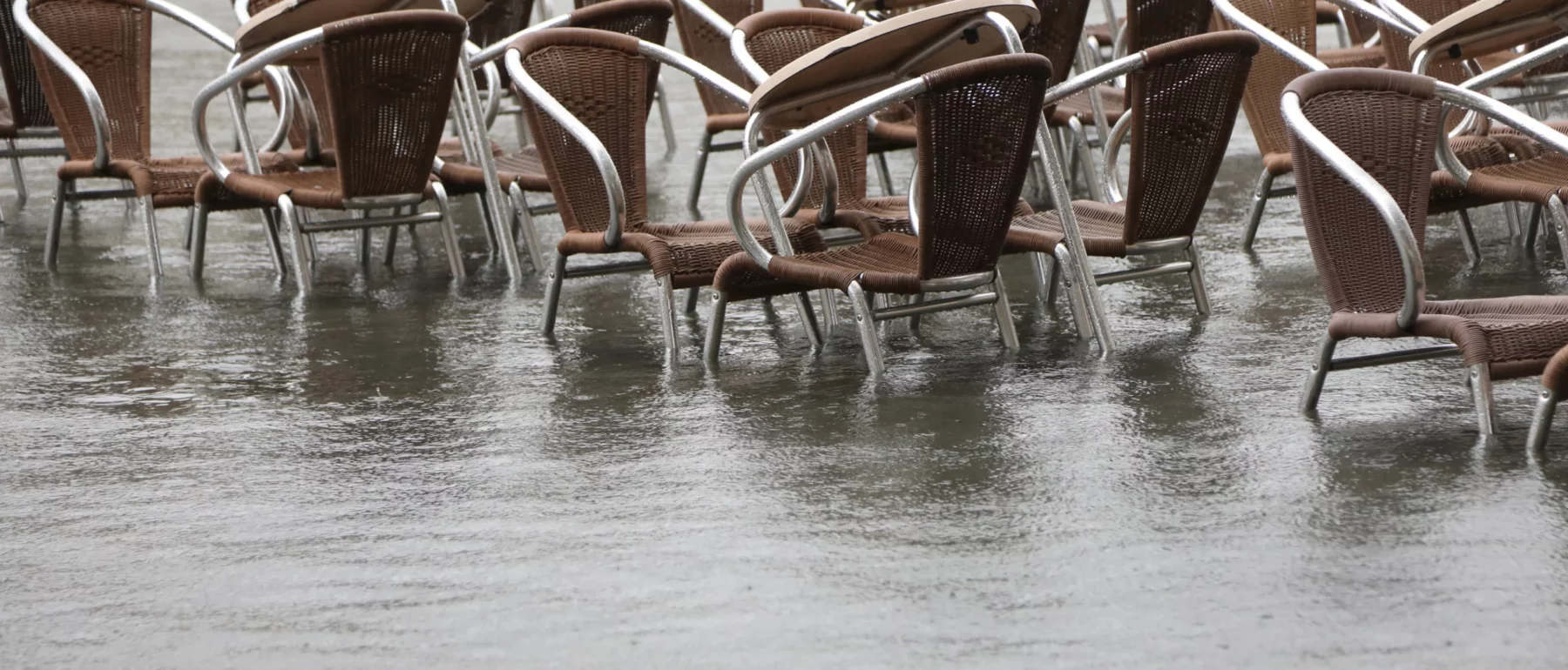 Flooded Venice with a lineup of empty chairs partially submerged in water, highlighting the impact of high tide events.