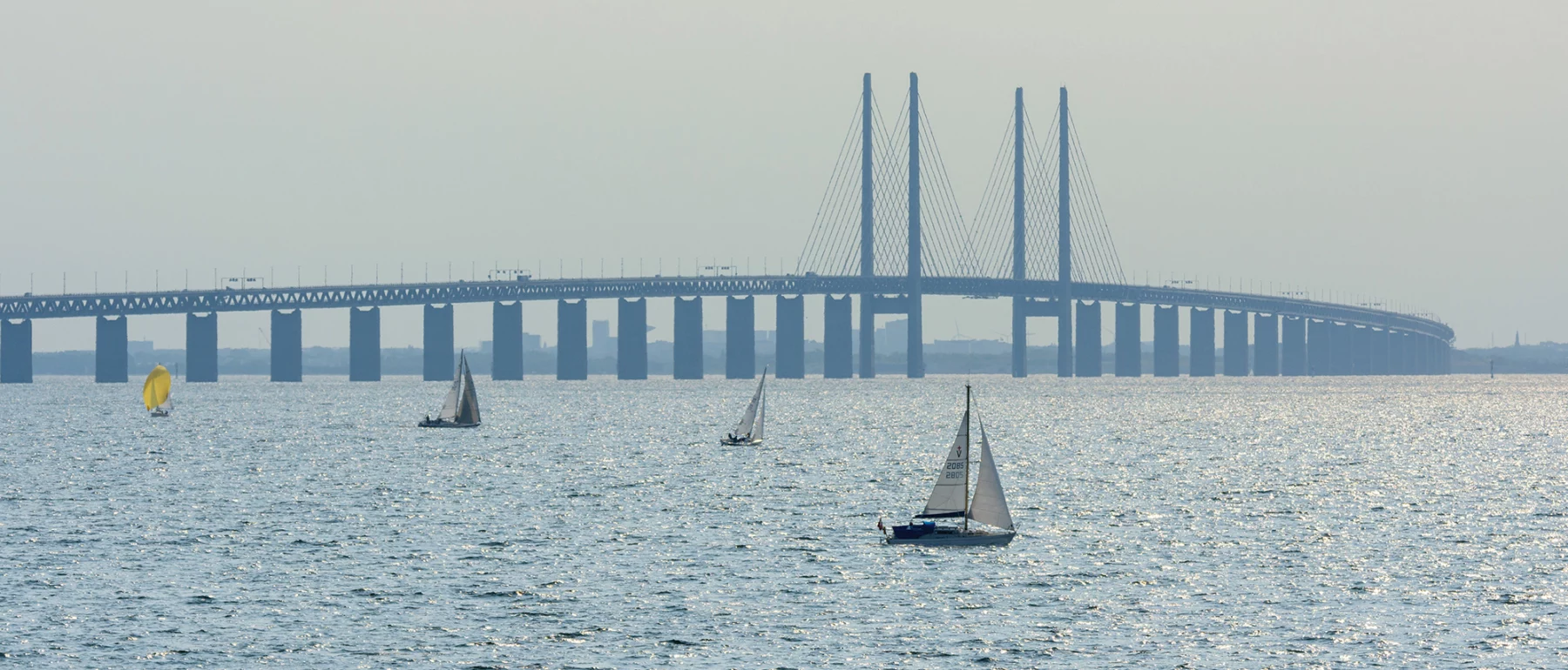 Oresund Bridge, Sealand, Denmark with ships sailing in the foreground on a sunny day.