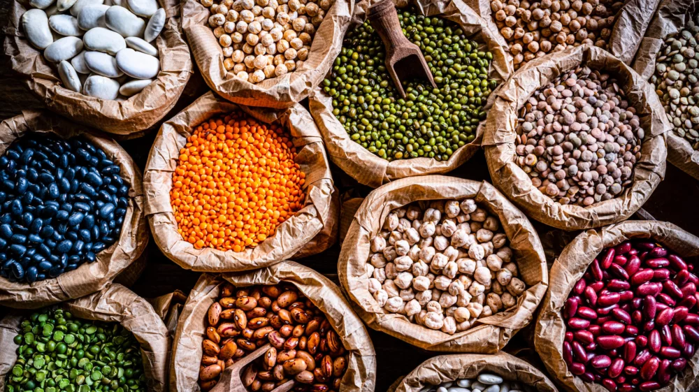 Dried beans and legumes of different colours in sacks, taken from above: black beans, green peas, red kidney beans, chickpeas, pinto beans, large white beans...