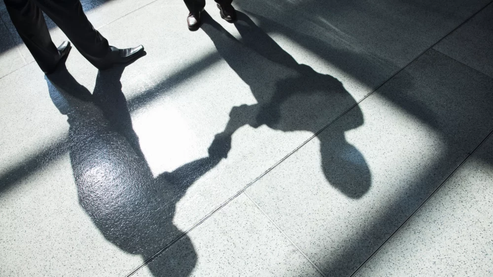 A shadow on a tiled floor of two businessmen shaking hands