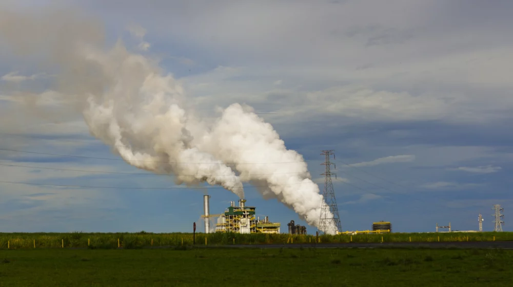 Open field with overhead wires and a factory producing steam or smoke.