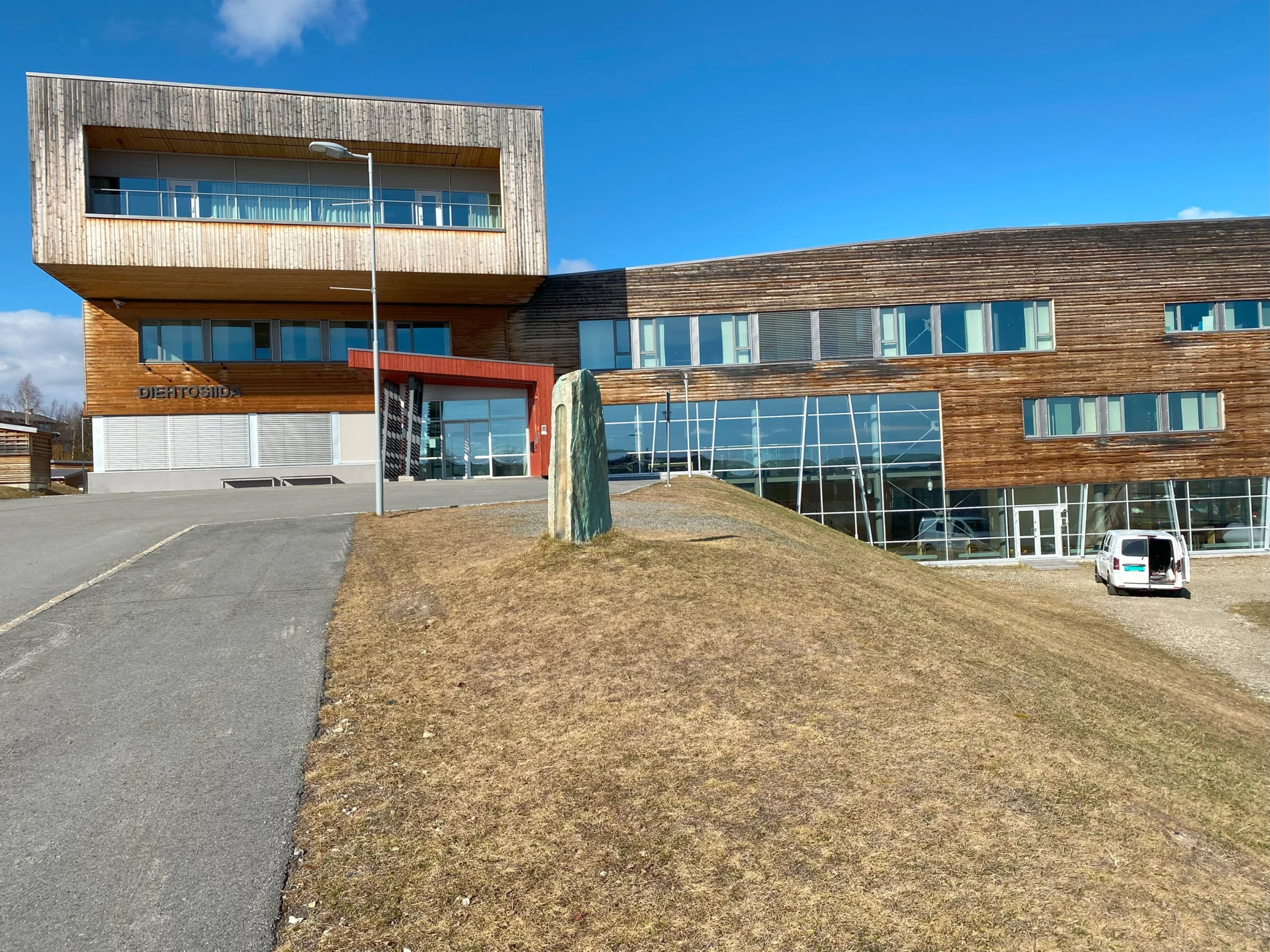 A modern wood and glass university building on a sunny day. Built on two levels with the entrance on a hill and the rest of the building on the lower level.