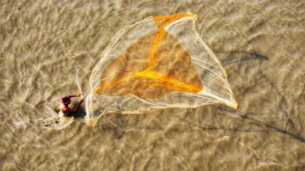Man casts fishing net across water