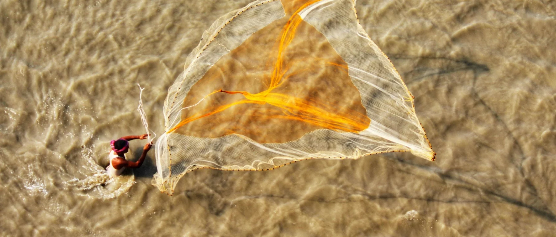 Man casts fishing net across water