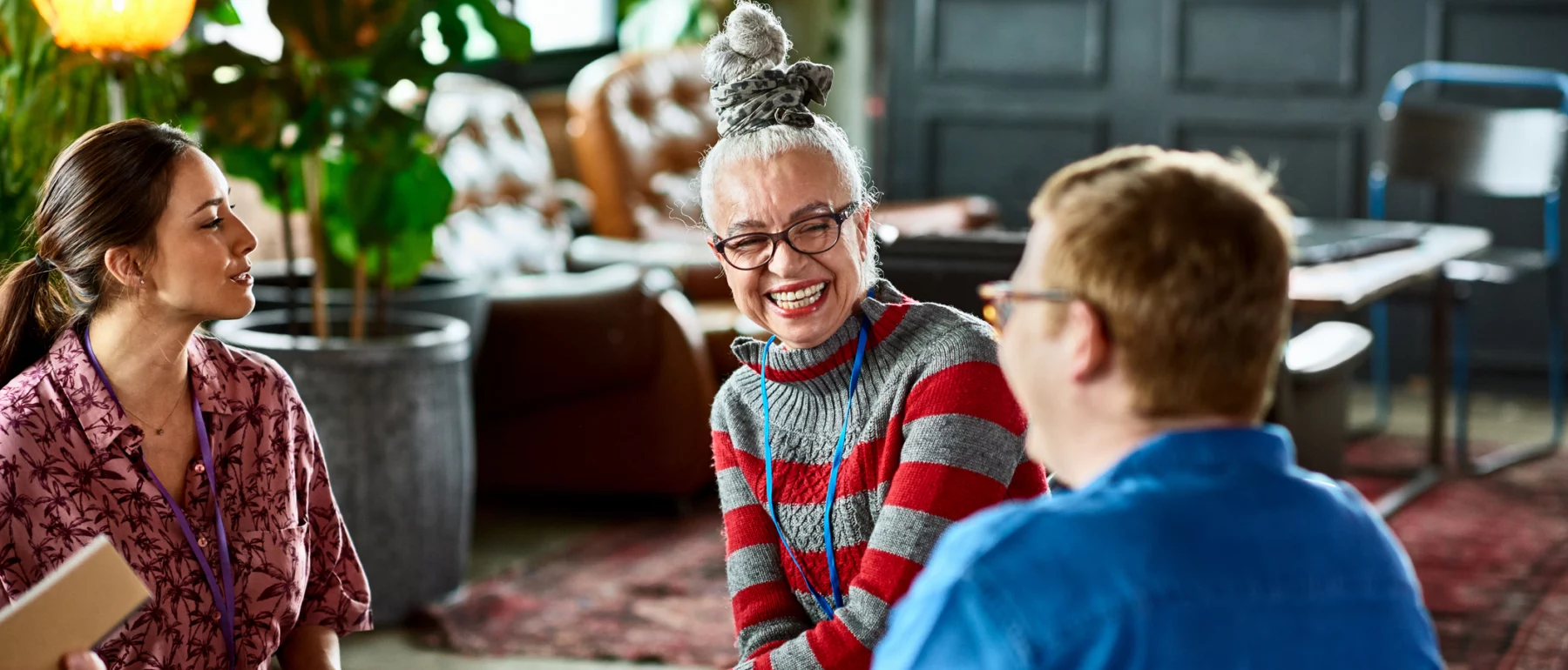 A stylishly dressed older woman laughs, as she sits in a group with other people.