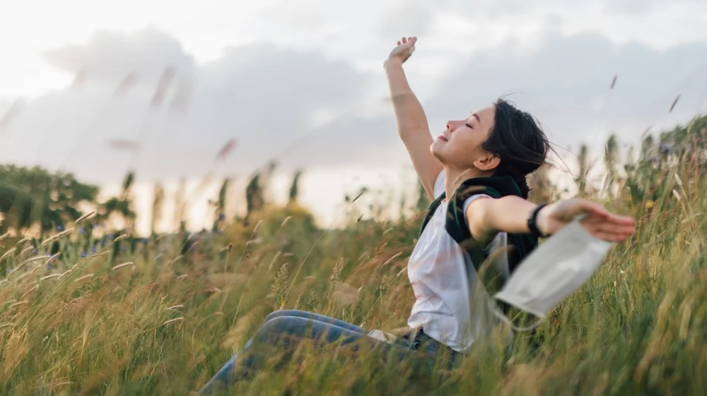 Beautiful young Asian woman removing protective face mask, relaxing at the park to reconnect wit nature
