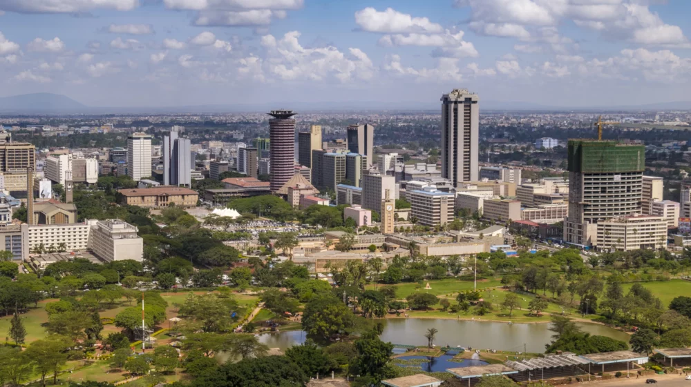 Skyline of Nairobi, Kenya, showing modern skyscrapers and lush greenery of Uhuru Park under a partly cloudy sky.