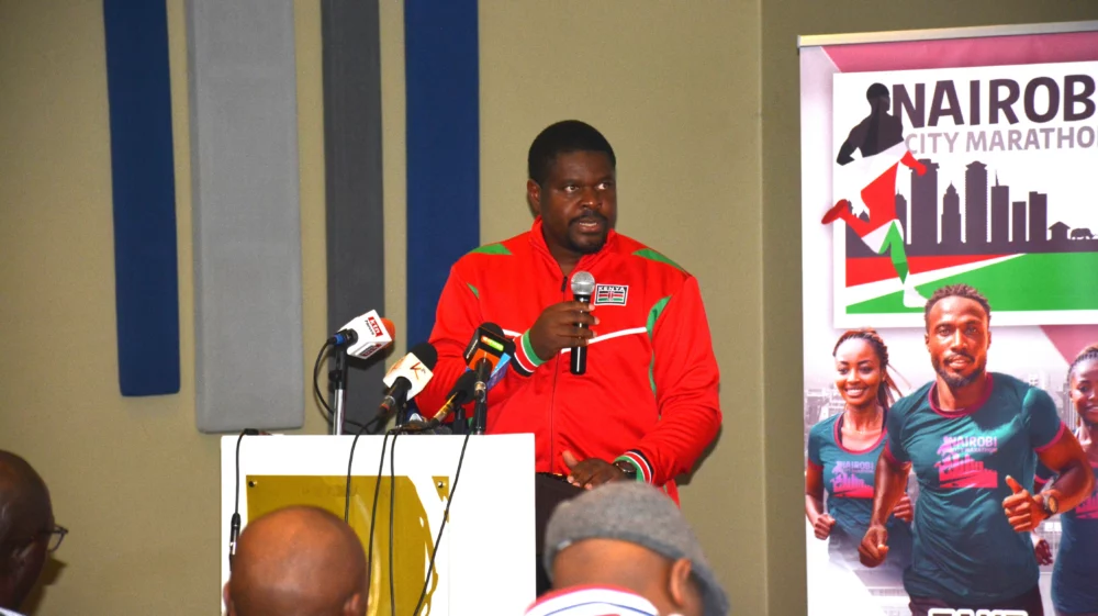 SEI Africa researcher Ngongang Danube speaks at a podium to the press, wearing a red jacket, with microphones in front of him and a Nairobi City Marathon banner in the background.
