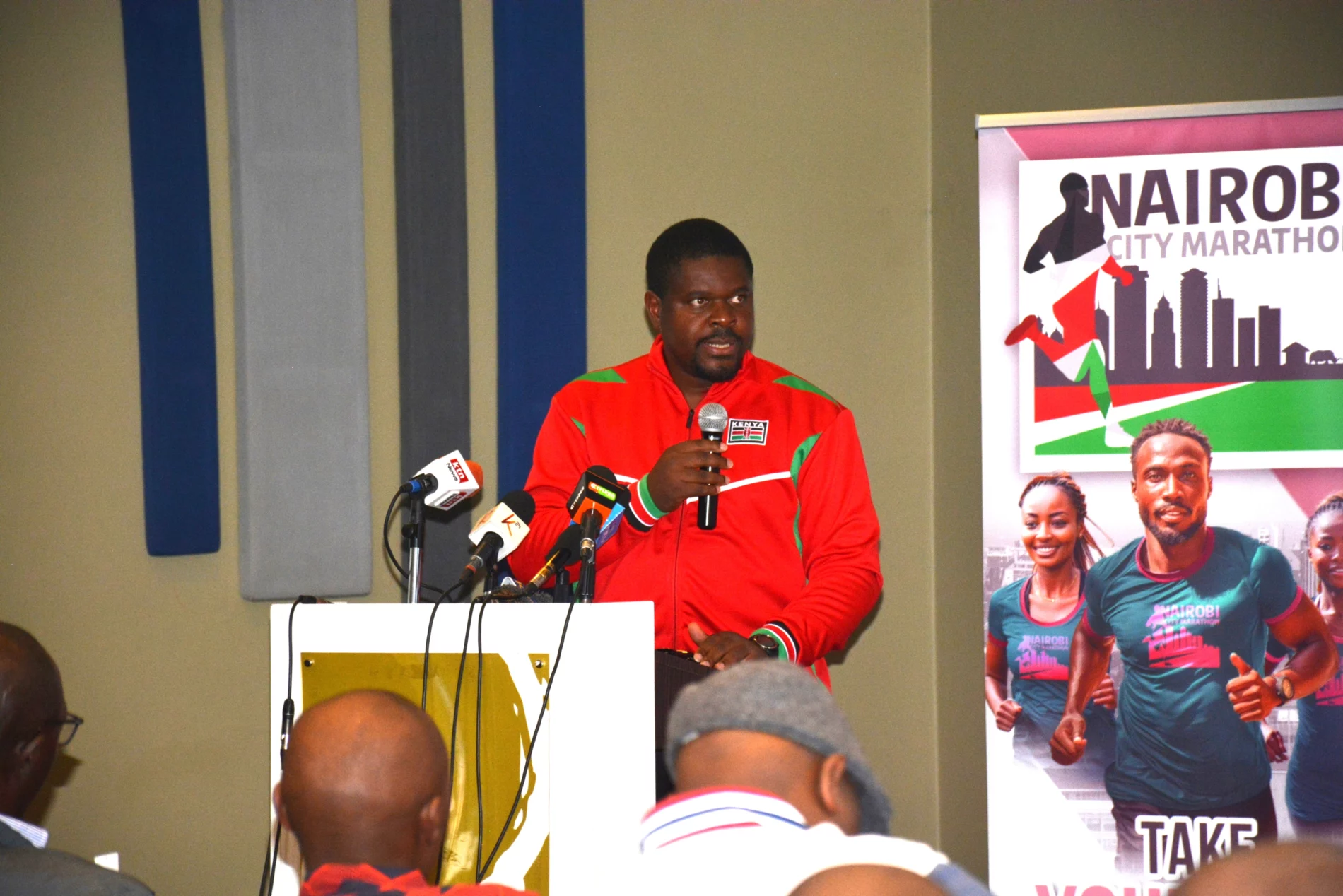 SEI Africa researcher Ngongang Danube speaks at a podium to the press, wearing a red jacket, with microphones in front of him and a Nairobi City Marathon banner in the background.