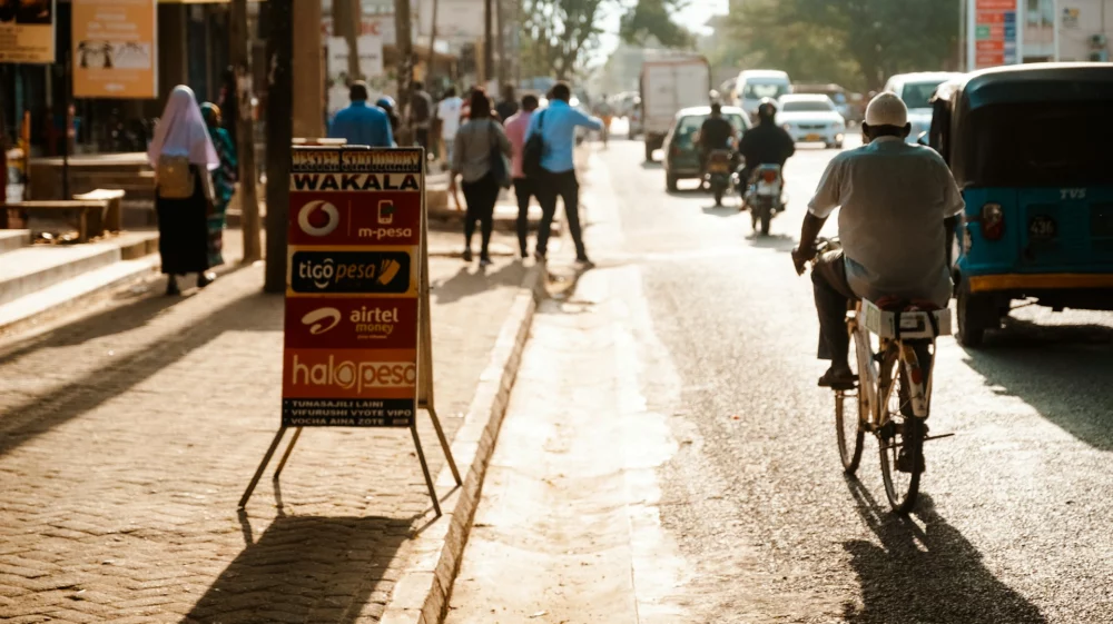 Landscape shot of a street. Traffic moves away from the camera. In the foreground is an older man on a bicycle.