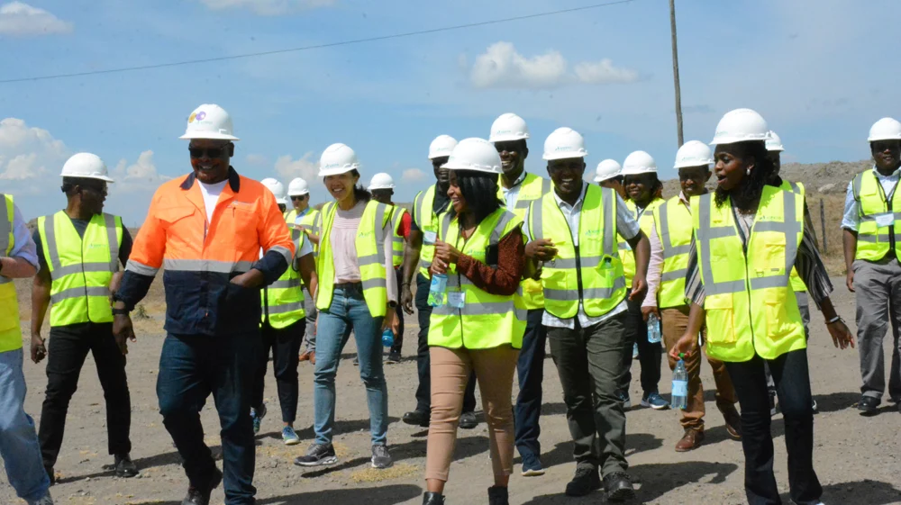 Group of workshop participants in high-visibility vests and hard hats walking together during a site visit to Kipeto Wind Farm, Kenya.