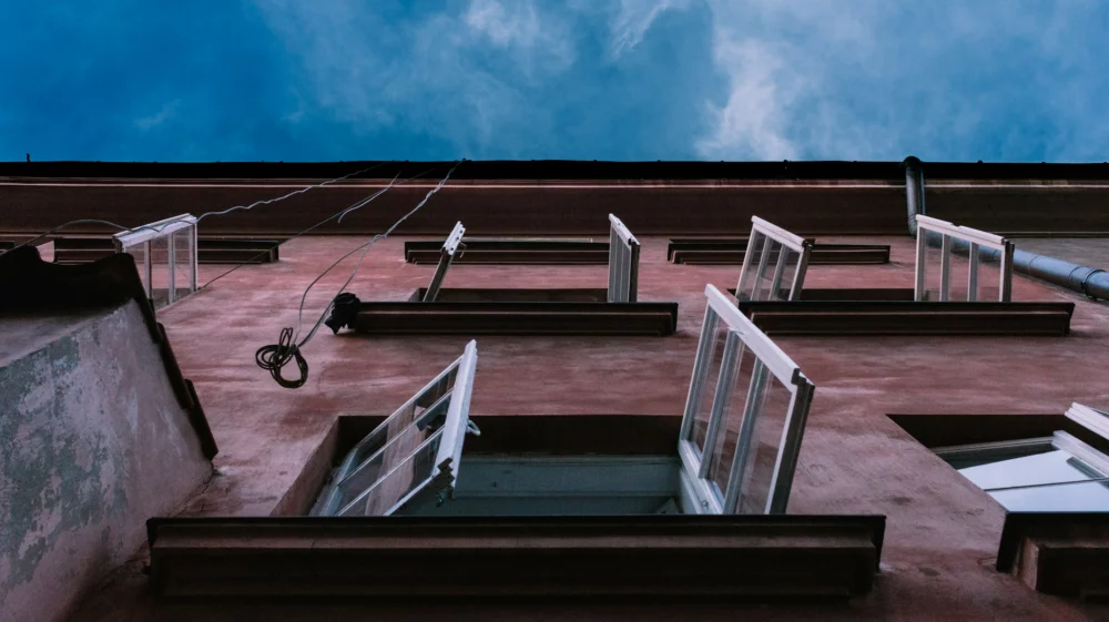 View looking up at a brick building with several open windows, from below