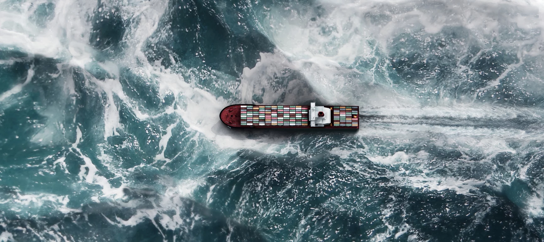 A view from above of a container ship with white capped waves crashing around it on an aquamarine sea surface.