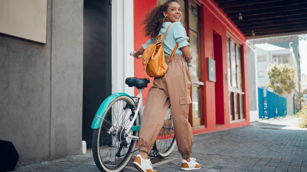 Happy, city and girl with a bicycle to travel to school, university or college to reduce carbon footprint outdoors. Smile, street and young student traveling or riding a cool bike in an urban town