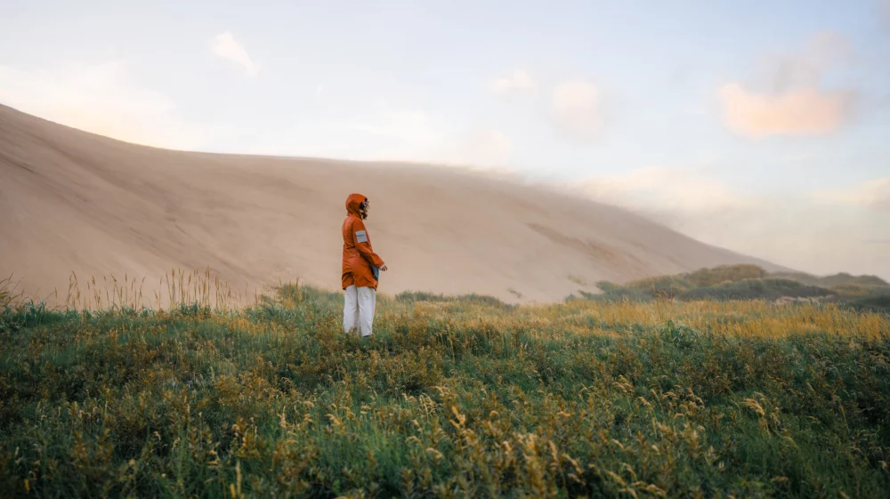 Young Caucasian woman walking near the big sand dunes in Denmark during extreme weather