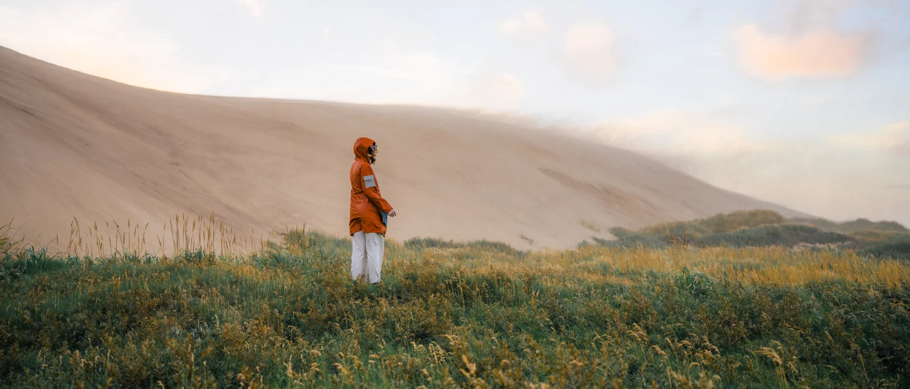 Young Caucasian woman walking near the big sand dunes in Denmark during extreme weather