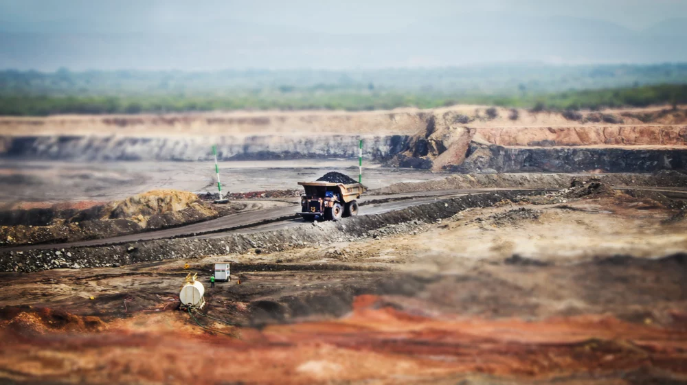 Tilt-shifted image of coal mining, with red dirt in the foreground and a truck carrying coal in focus in the middle ground