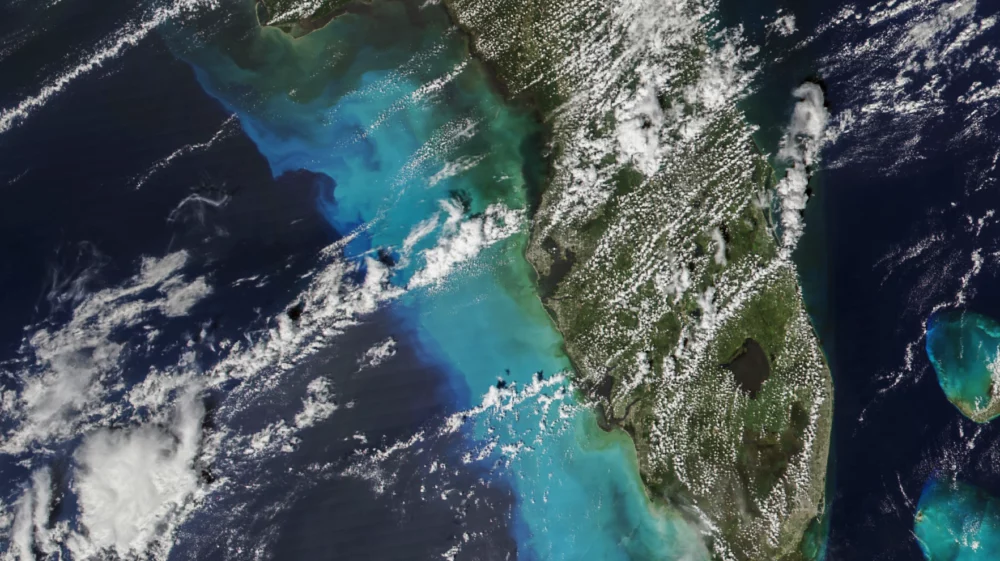 White swirls of clouds hange over the blue ocean and green land, where a hurricane is about to hit Florida.