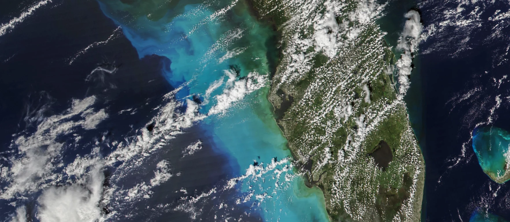 White swirls of clouds hange over the blue ocean and green land, where a hurricane is about to hit Florida.