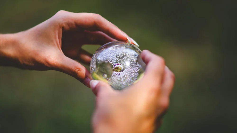 Close up of a woman's hands, holding a colourless glass ball filled with air bubbles, akin to a crystal ball.