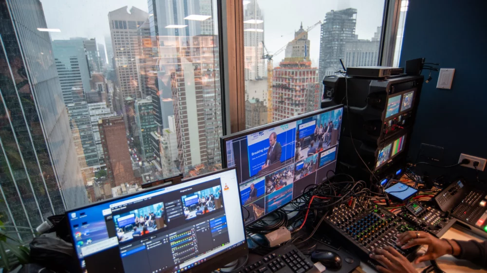 The view through a window in a skyscraper in the NewYork looking across the skyline. In the foreground there is a livestream audio and video mixing desk.