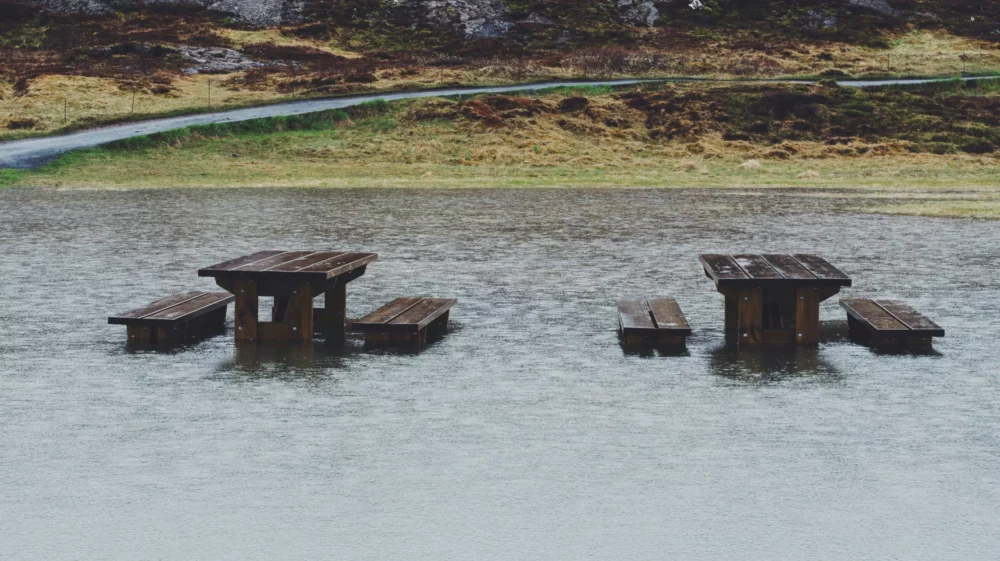 Brown wooden picnic tables half covered by flood water