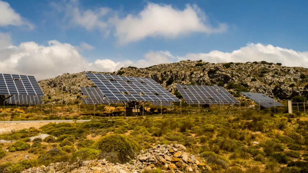 solar panels on a rocky hill, with a road and chain fencing.