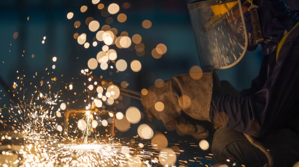 Glowing hot white and gold sparks fly as a worker with a welding mask, heavy gloves and tool leans in to the surface.