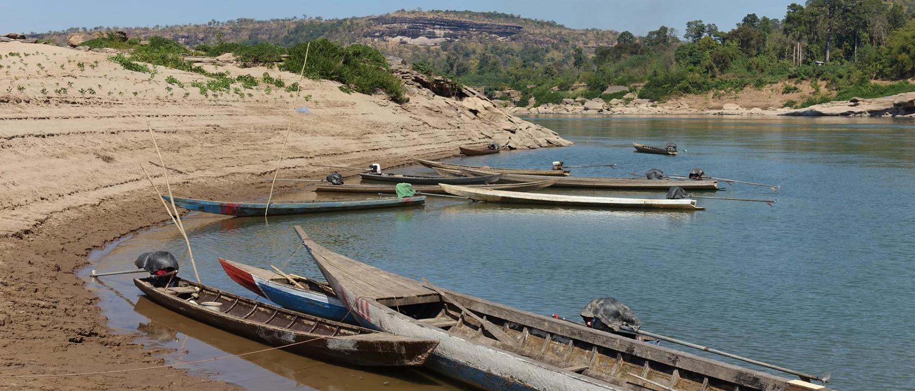 A group of fishing boats sit along the bank of a river