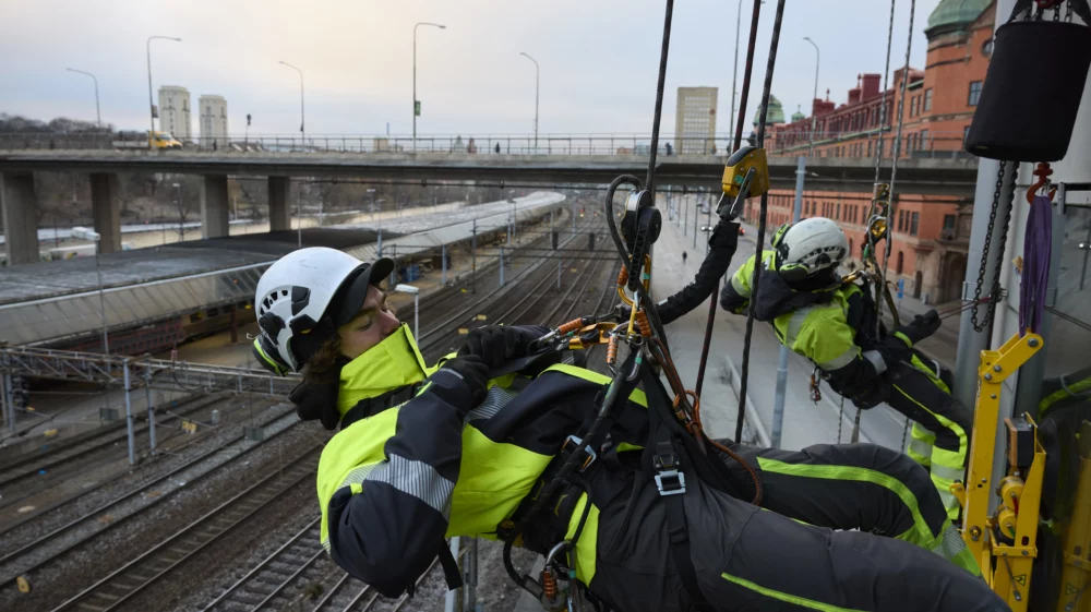 Rope access worker fastening carabiner to rope while hanging from building.