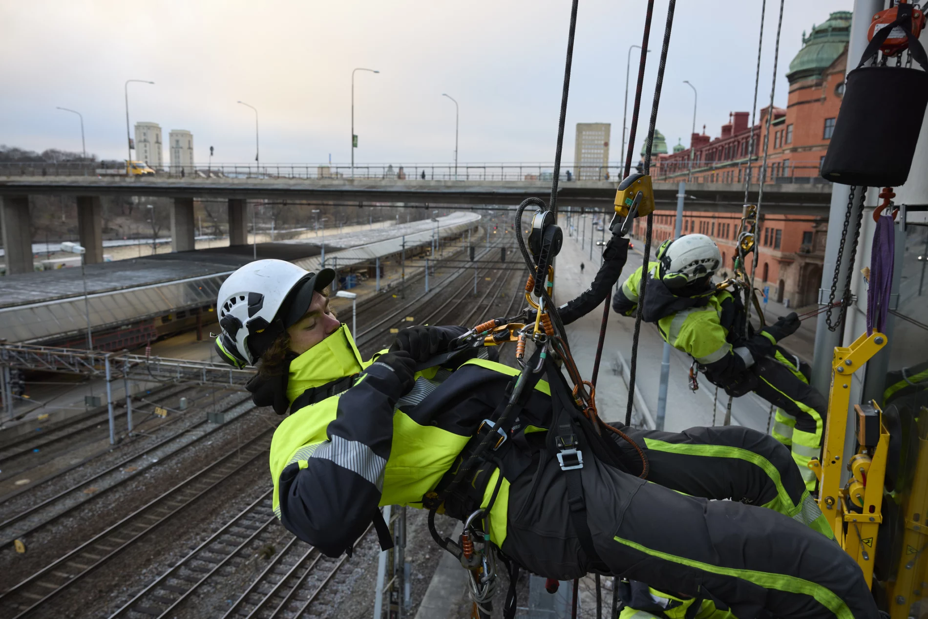 Rope access worker fastening carabiner to rope while hanging from building.