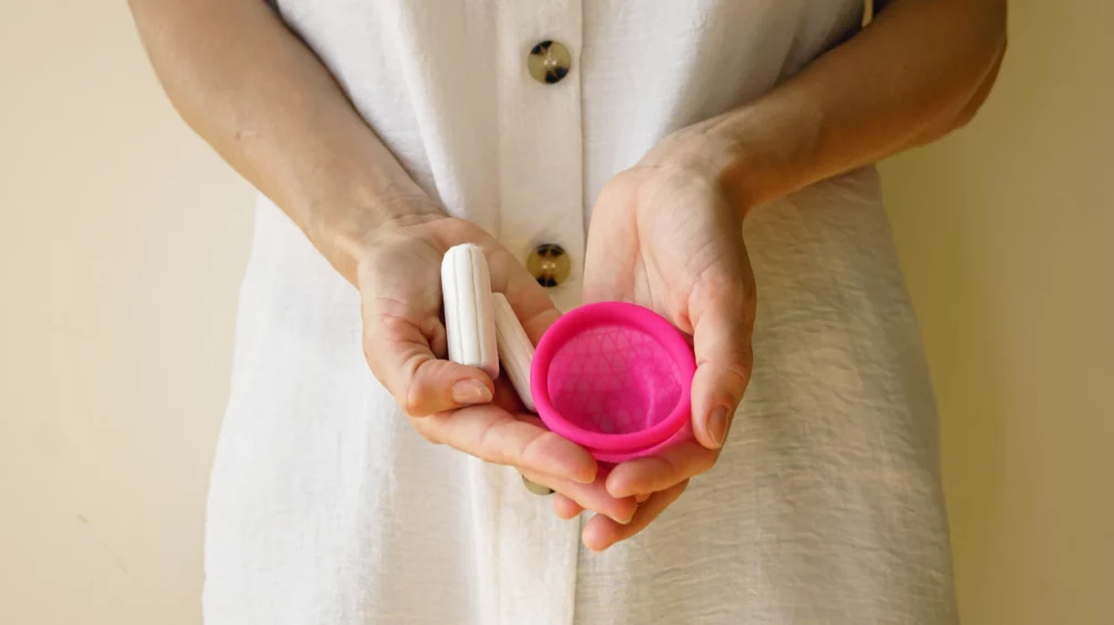 A close up image of a person holding tampons and a menstrual cup