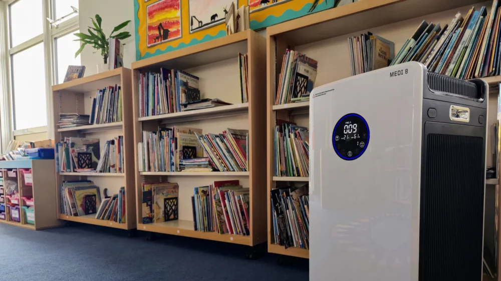 HEPA filter unit in a school classroom with bookshelves and children's artwork in the background.