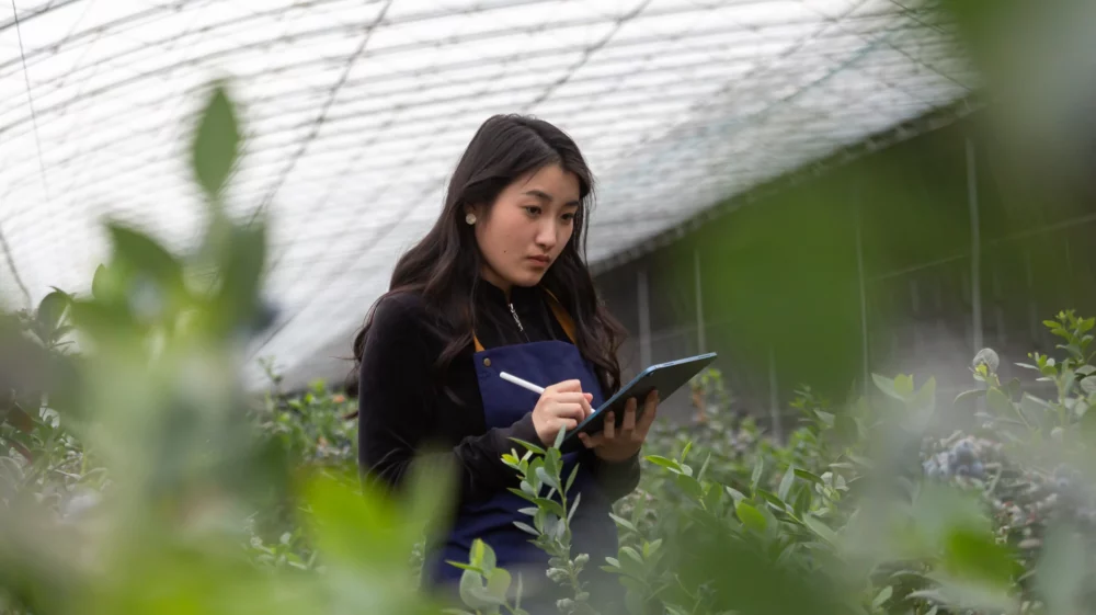 young asian woman using digital tablet in a greenhouse with plants all around
