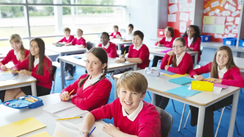 Pupils in school uniform sitting desks in a classroom.