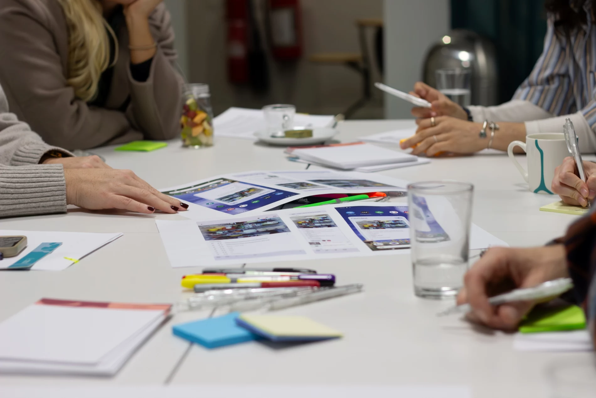 View of a desktop with illustrations, colourful post it notes, pens, surrounded by people discussing
