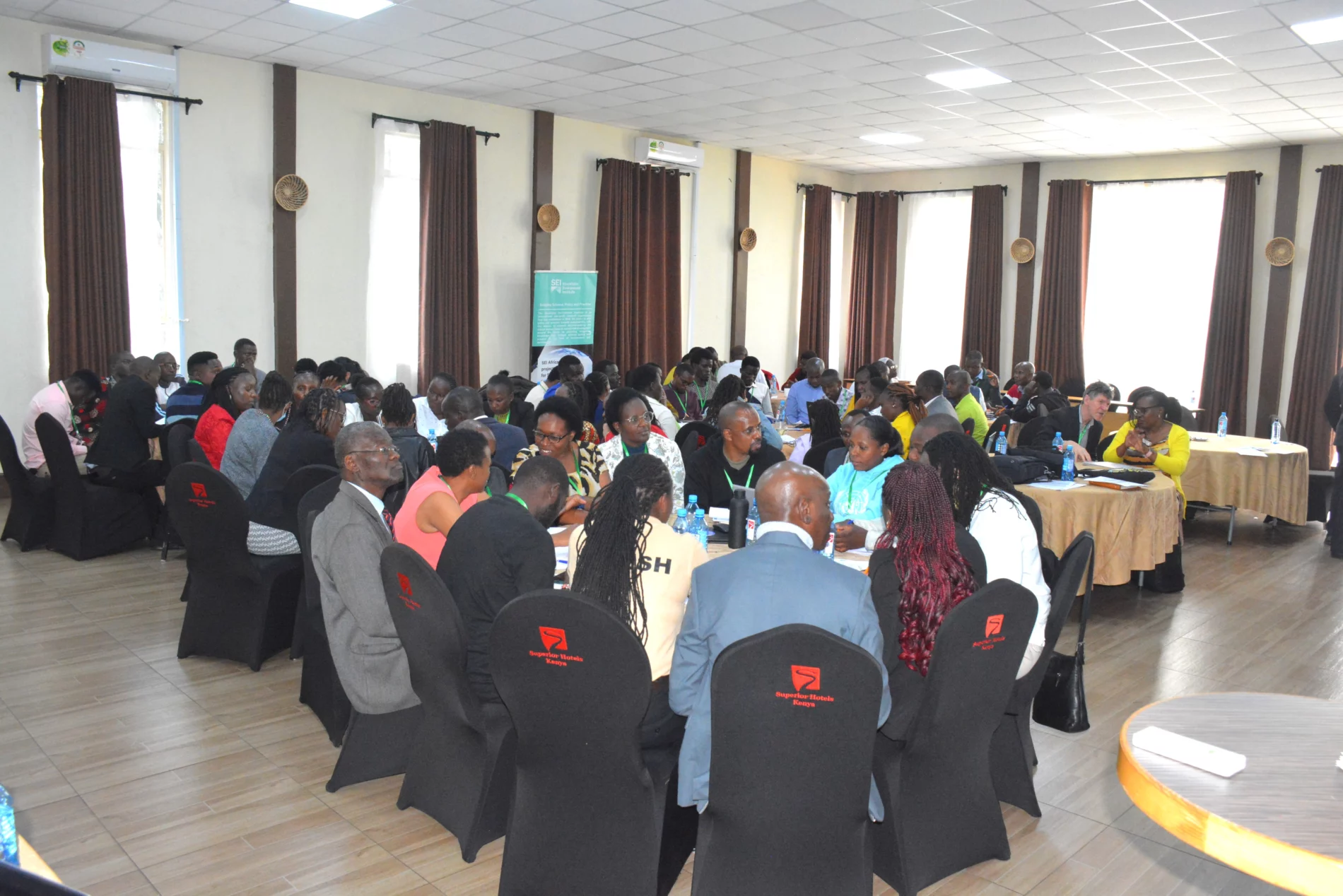 A diverse group of participants engaged in discussions during a workshop on Kenya’s bioeconomy. Attendees from various sectors, including agriculture, energy, and waste management, are seated in groups, exchanging insights on policy, finance, and innovation opportunities.
