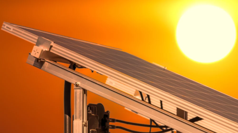 Tilted solar panel beneath a setting sun against a dark orange sky
