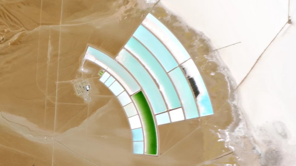 An overhead view of lithium ponds, light blue and green in sharp arcs, on a tan desert surface.