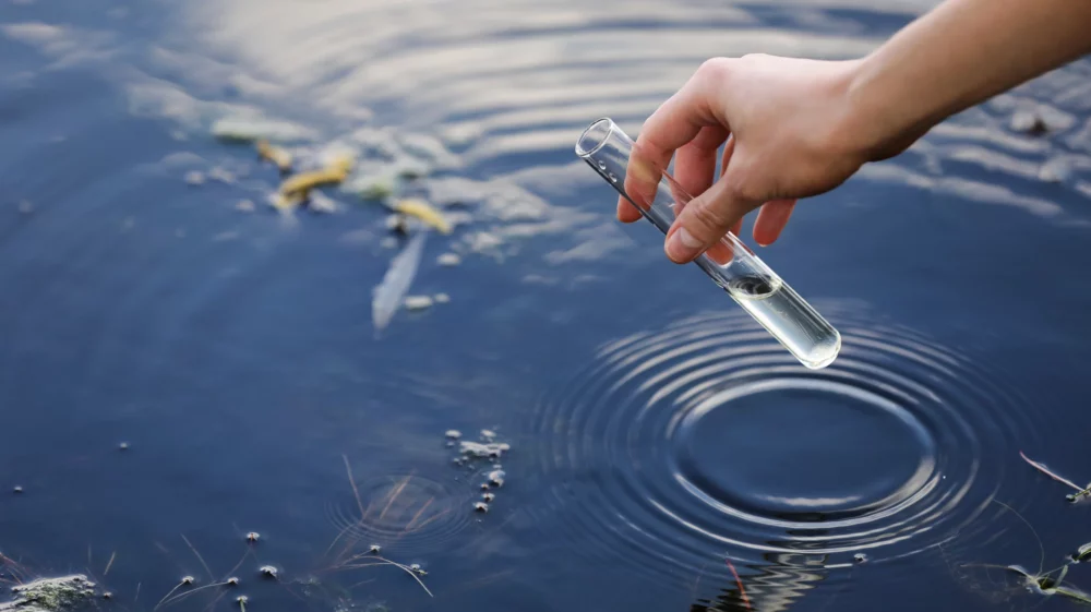 A hand draws water into a flask from a river.