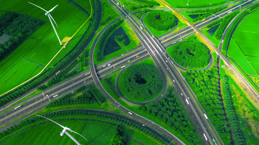 Drone view of intricate motorway junction with windmills against a backdrop of green fields.
