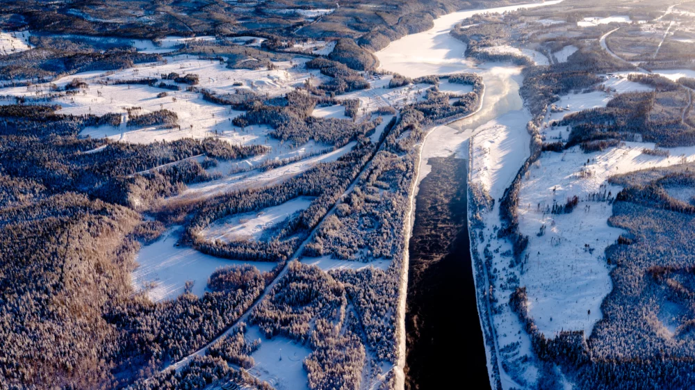 Birds eye view of a river flowing through a forested area with patches of snow