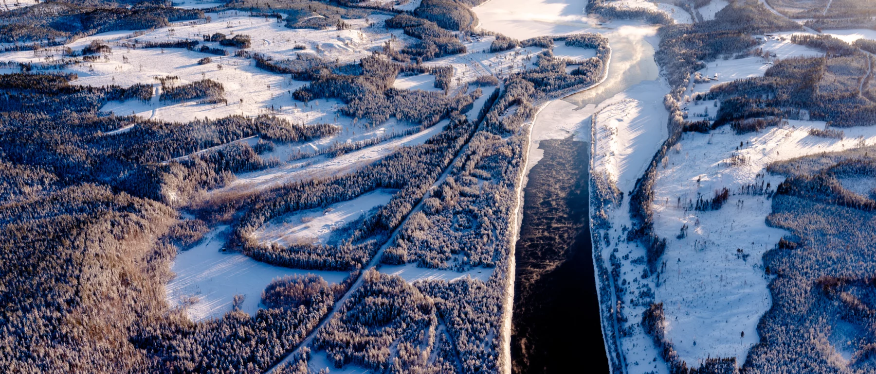 Birds eye view of a river flowing through a forested area with patches of snow