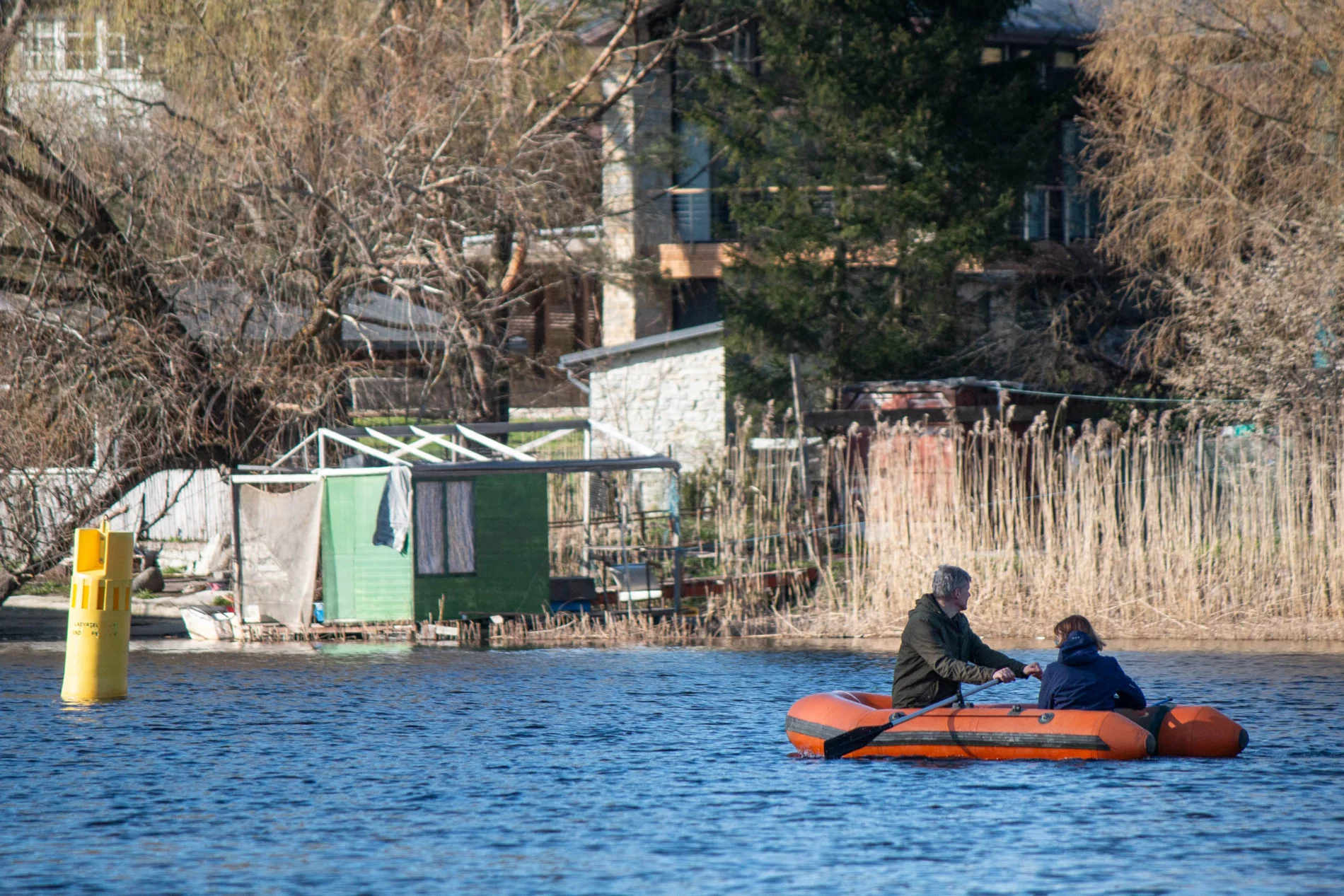 A man and a woman on a paddling boat on a city river with houses in the background.