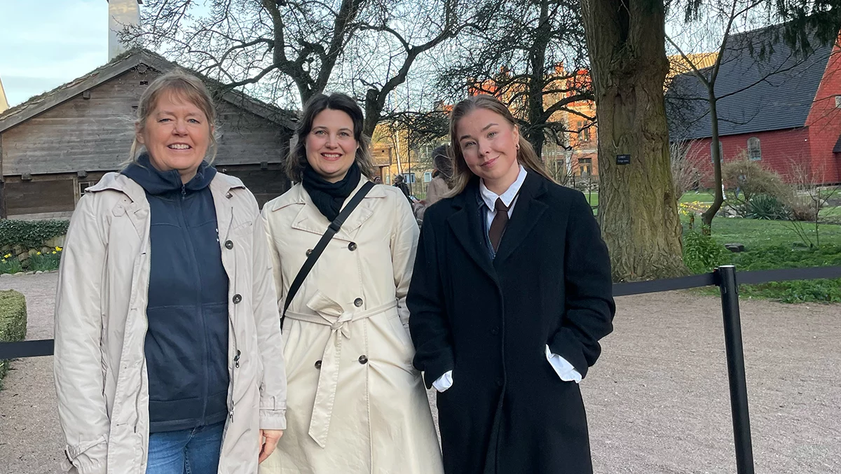 Katarina Axelsson, Karin André and Julia Jokiaho standing outdoors, smiling, with historic buildings and trees in the background.