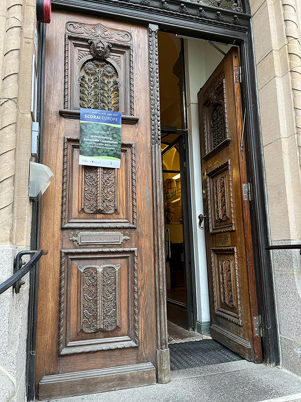 Ornate wooden doors propped open, with a SCORAI Europe conference poster displayed on one door panel.
