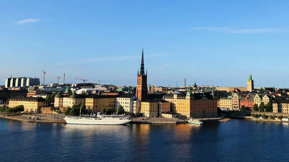 View of Stockholm’s historic waterfront with colorful buildings, church spires, and a blue sky above.