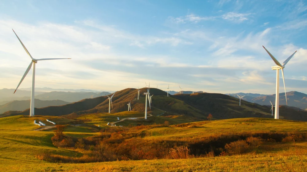Windmills dot rolling grassy hills under a blue sky with wispy white clouds