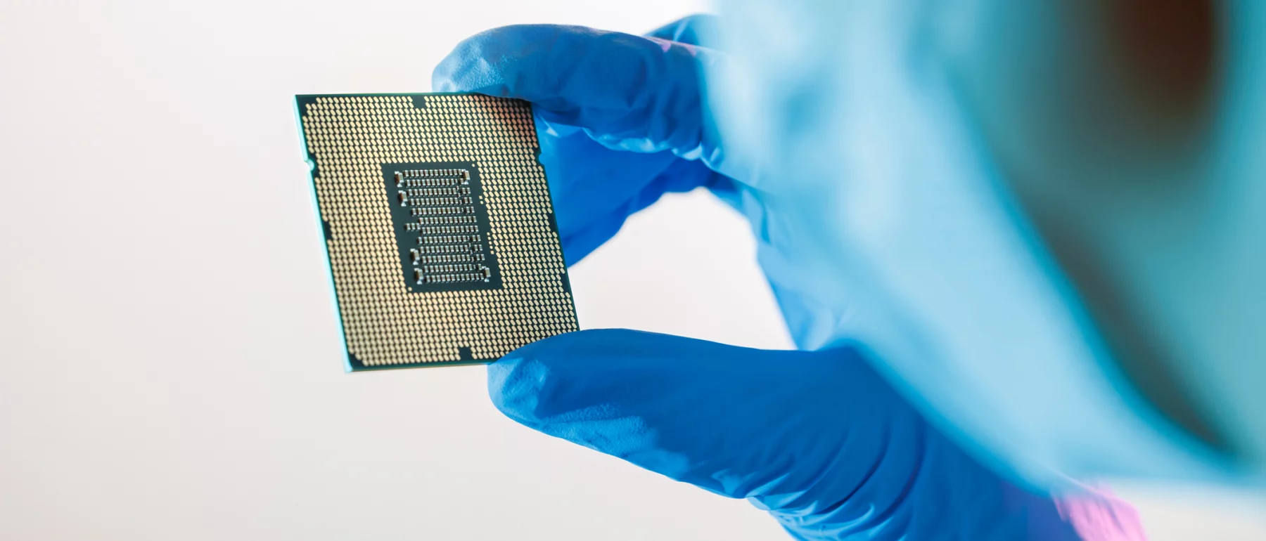 Close-up shot of a female Chinese factory worker wearing a mask and holding a CPU microchip and examining it.